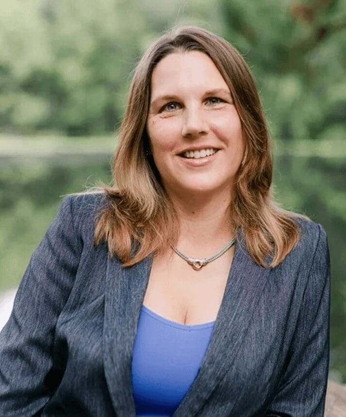 A woman in a blue top and jacket smiling.