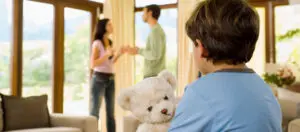 A boy is holding a teddy bear while two people are talking to him.